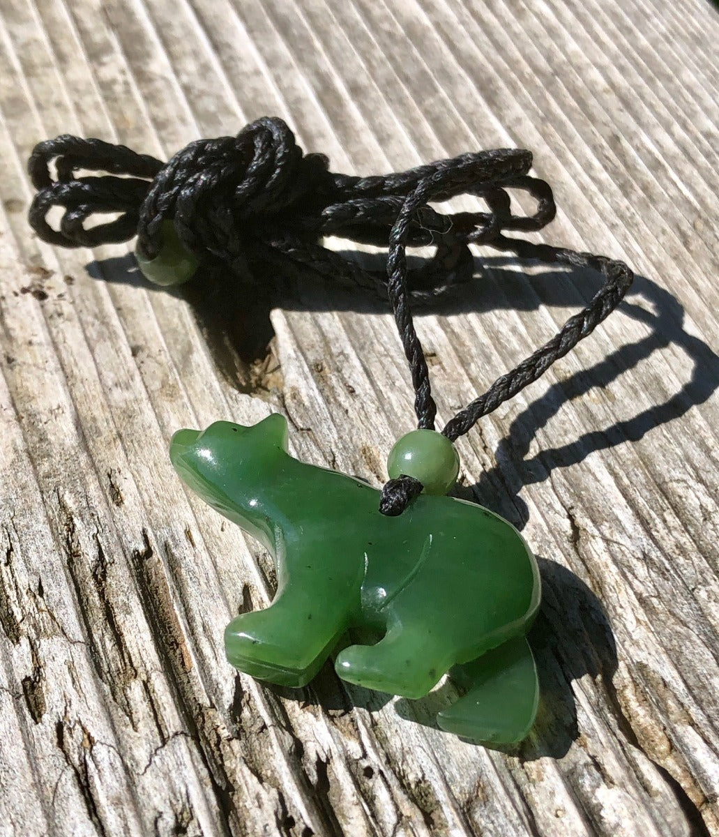 Close up of green jade bear pendant on black cord resting on weathered wood
