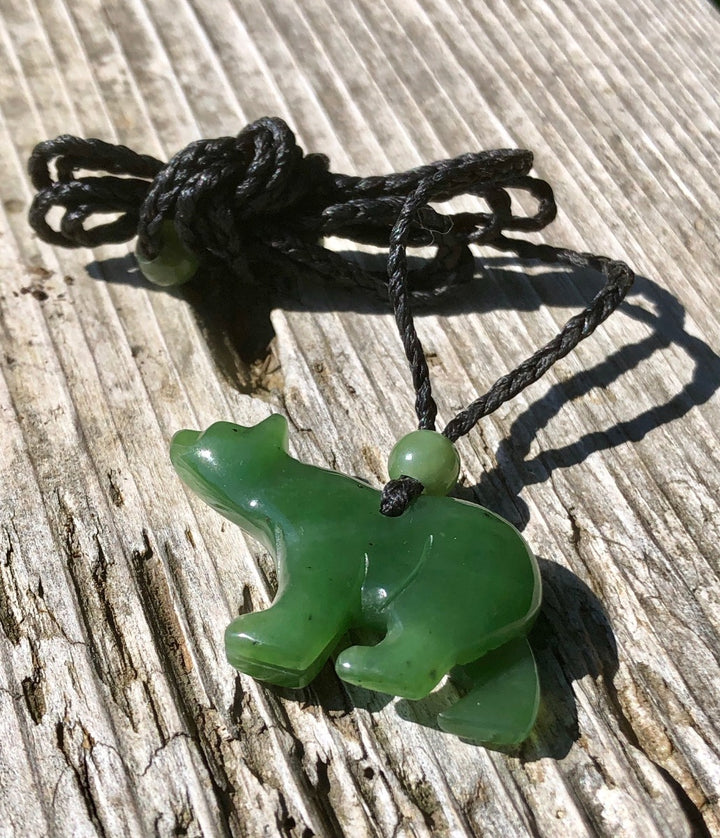 Close up of green jade bear pendant on black cord resting on weathered wood