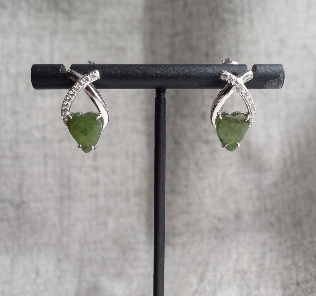 Pair of green teardrop earrings on a black stand against a gray background