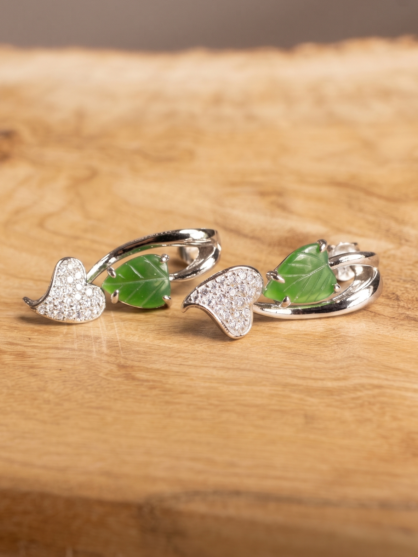 Silver leaf-shaped earrings with green leaves on a wooden surface, branded 
