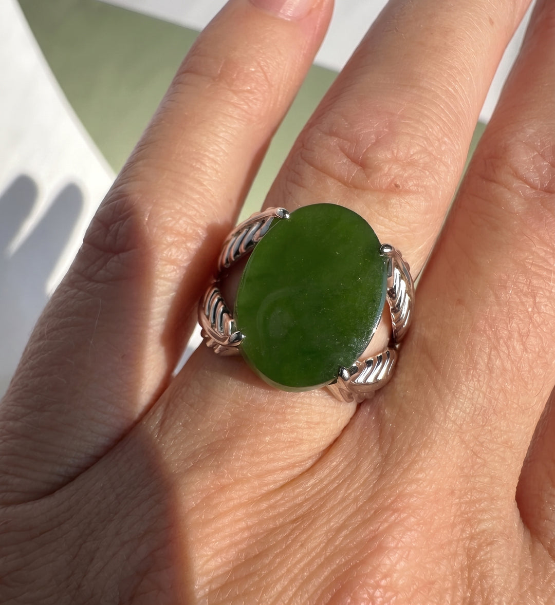 A close-up of a hand wearing a silver ring with a large, polished green stone.