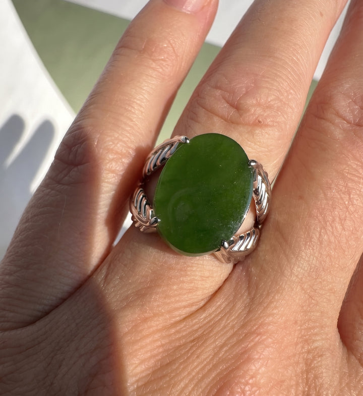 A close-up of a hand wearing a silver ring with a large, polished green stone.