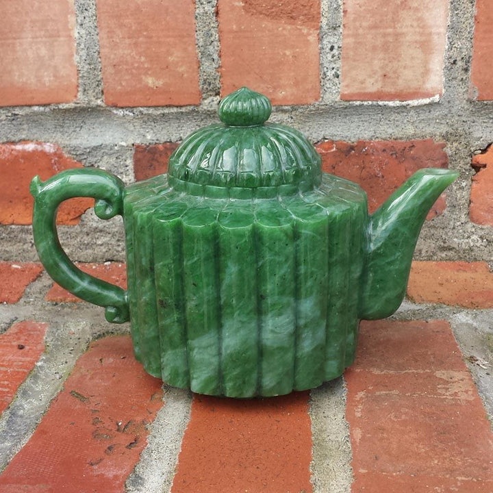 Green jade teapot with ribbed vertical body and lid on a brick surface.