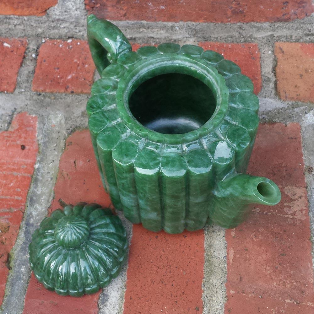Top view of jade teapot showing a ribbed surface, open top, spout to the right, and lid nearby.