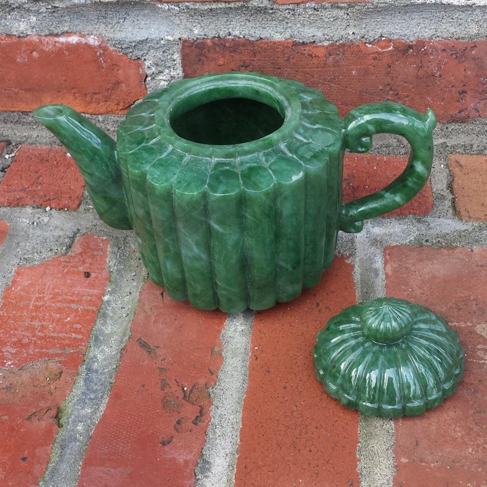 Jade teapot with a ribbed round body and spout on the left, handle on the right, lid resting beside on a brick surface.