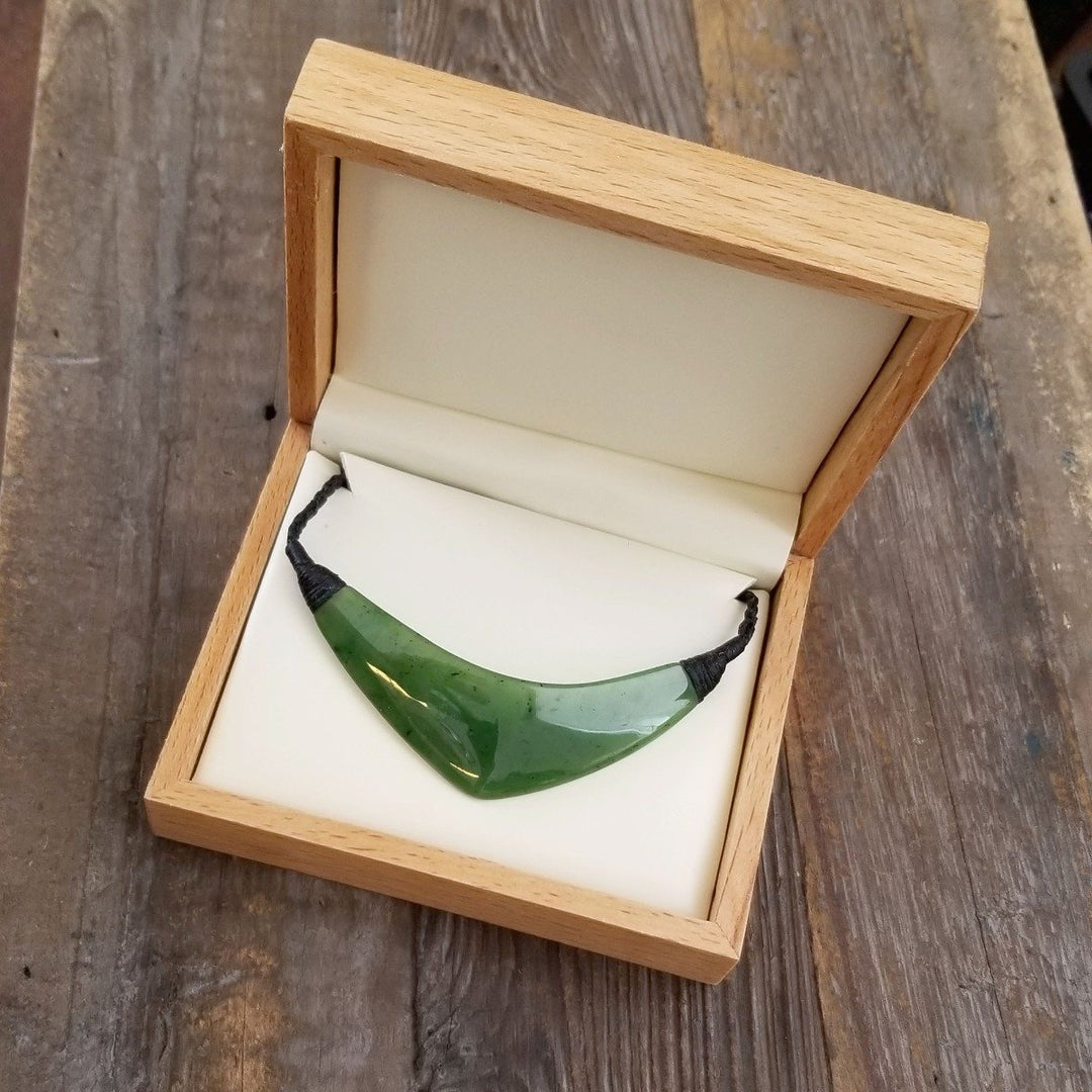 Jade pendant displayed in an open wooden box with white interior on a rustic wooden surface.