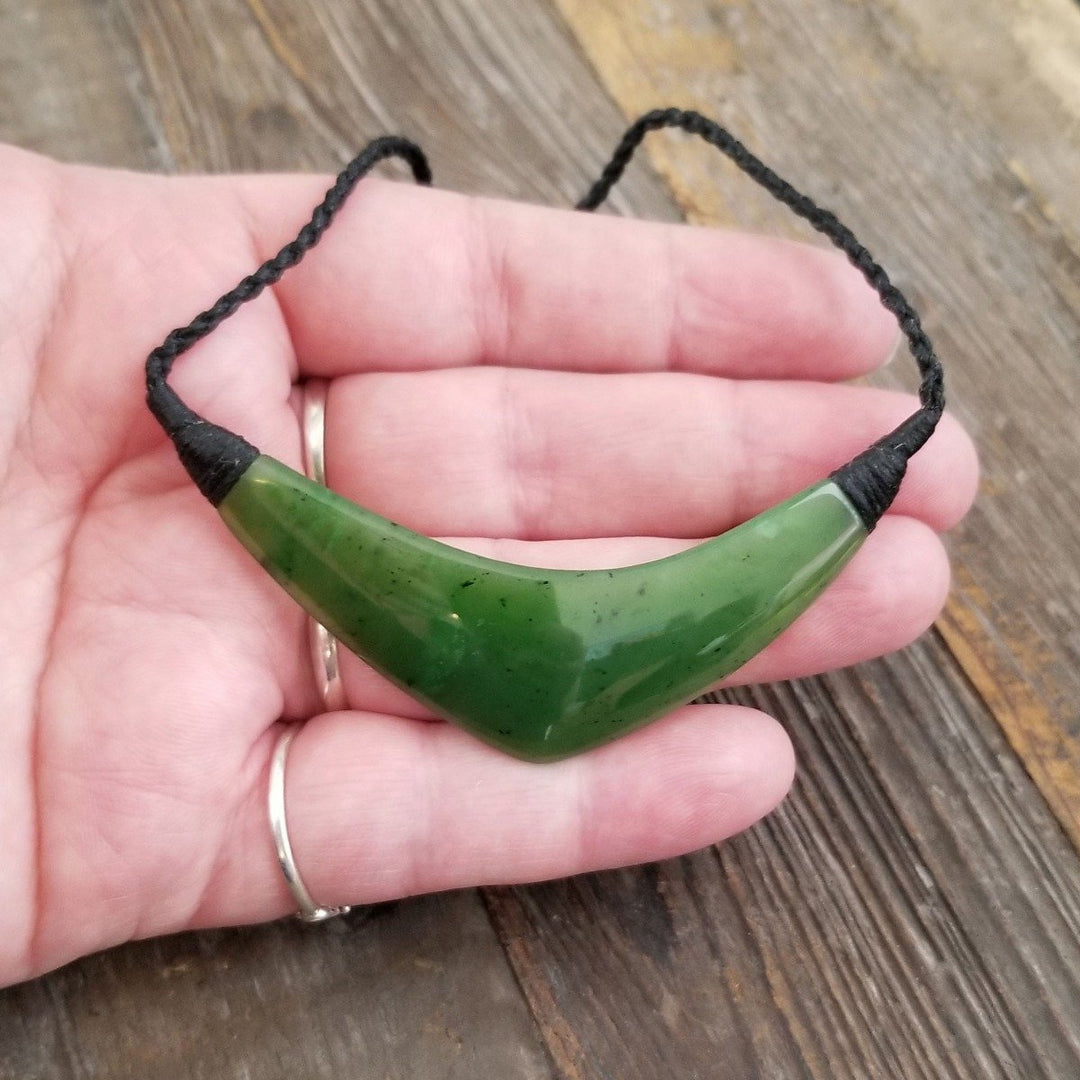 Hand holding a curved green jade pendant on a black cord necklace