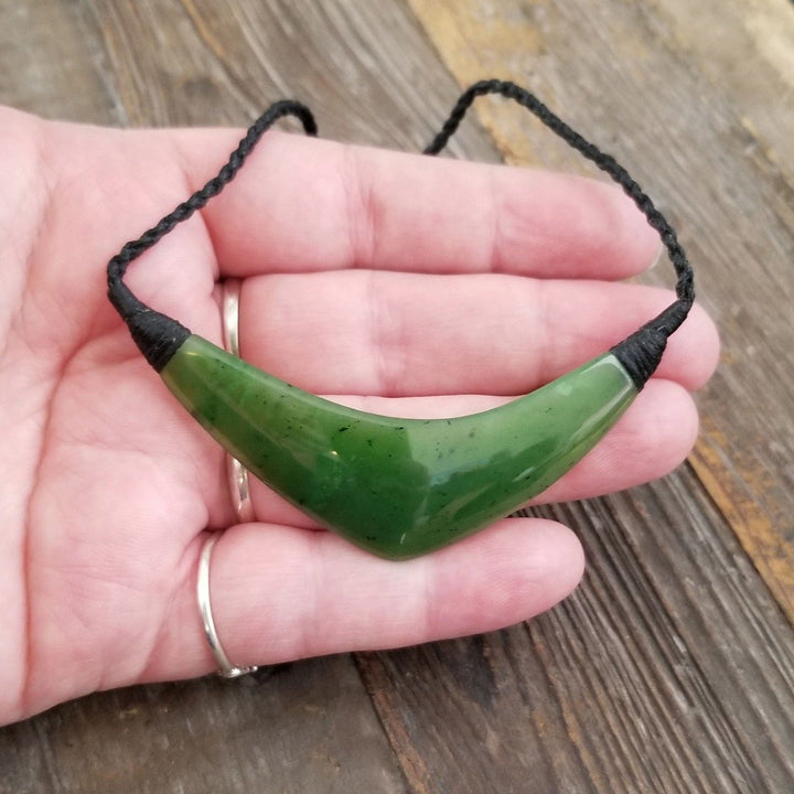 Hand holding a curved green jade pendant on a black cord necklace