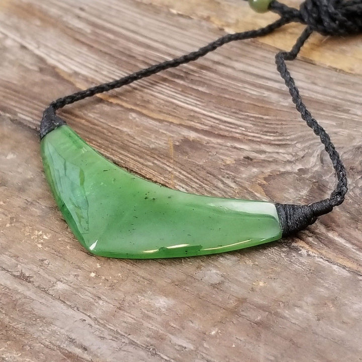 Green jade cheveron style pendant on black cord, on a rough wooden surface
