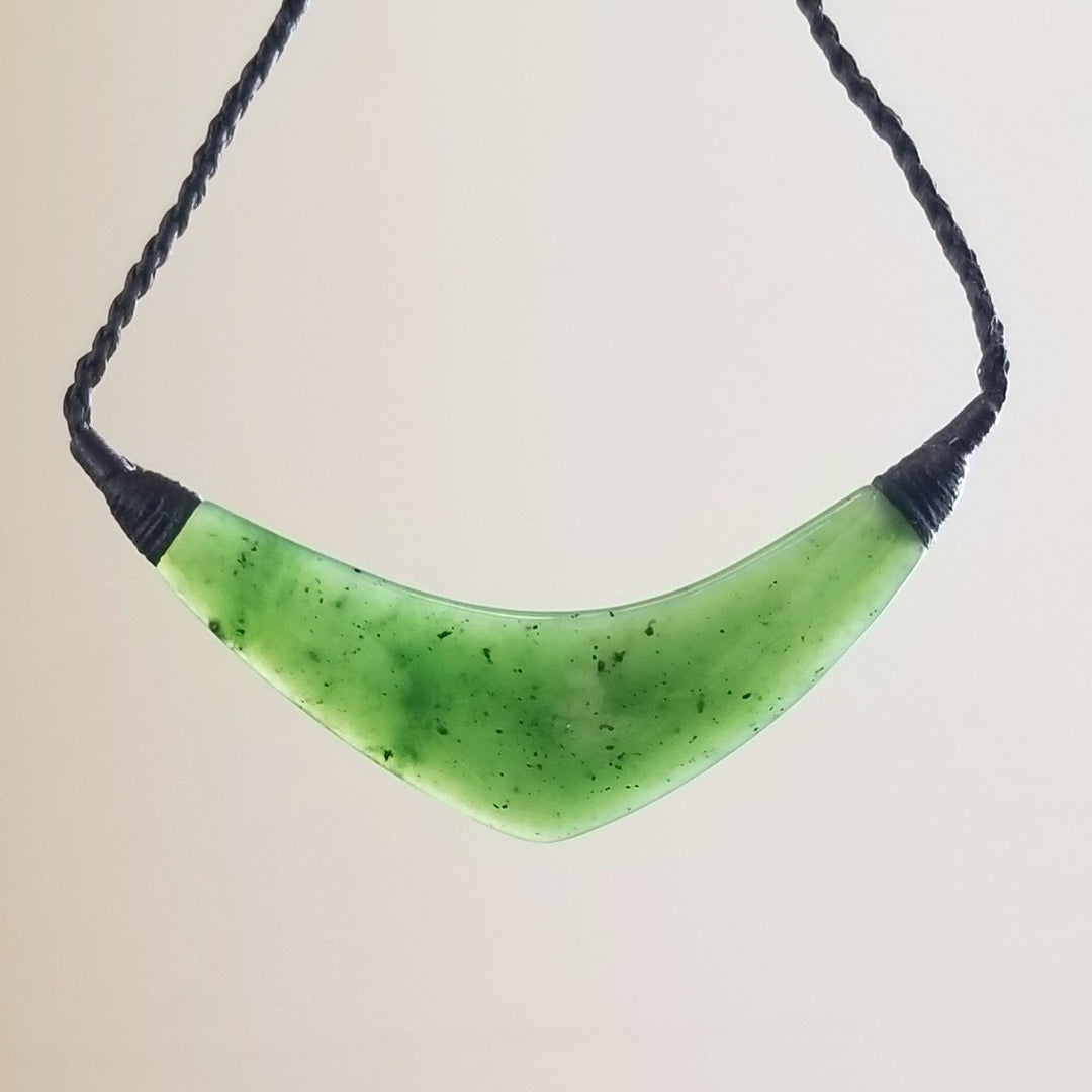 Green jade crescent pendant suspended on a black braided cord against a white background
