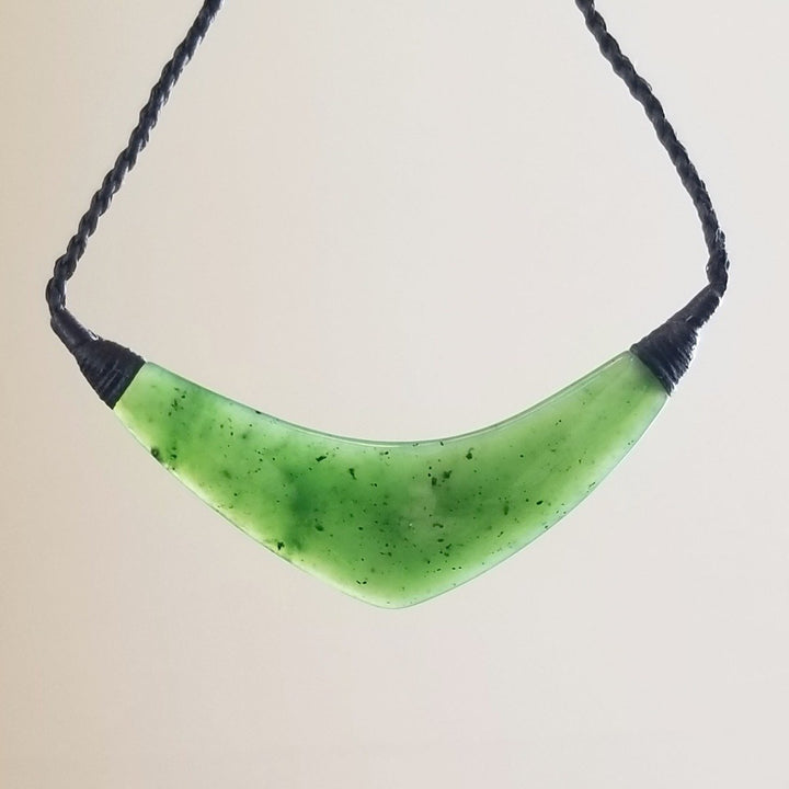 Green jade crescent pendant suspended on a black braided cord against a white background