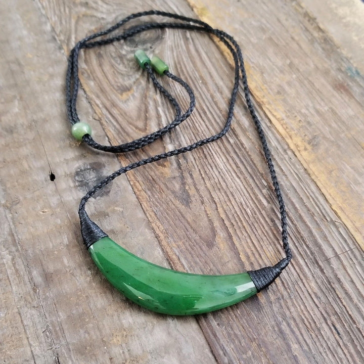 Curved green jade pendant on a black braided cord with green bead accents