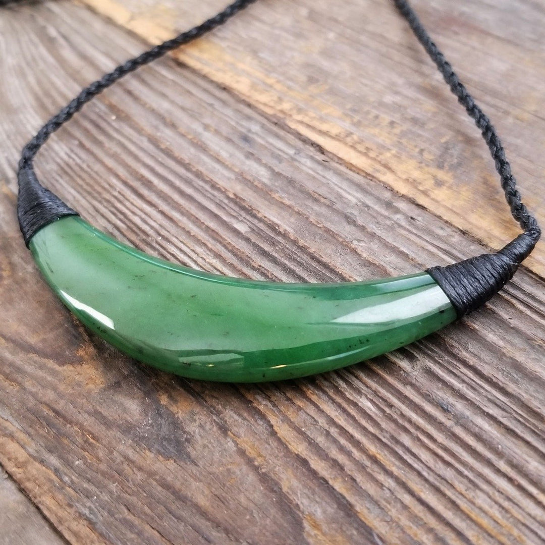 Curved green jade pendant on a black braided cord