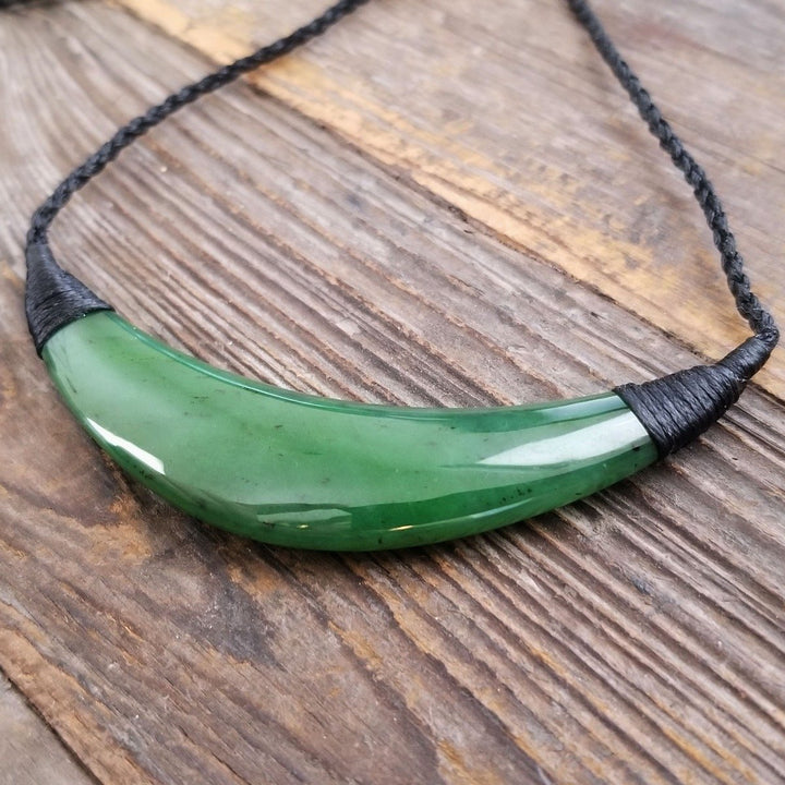 Curved green jade pendant on a black braided cord