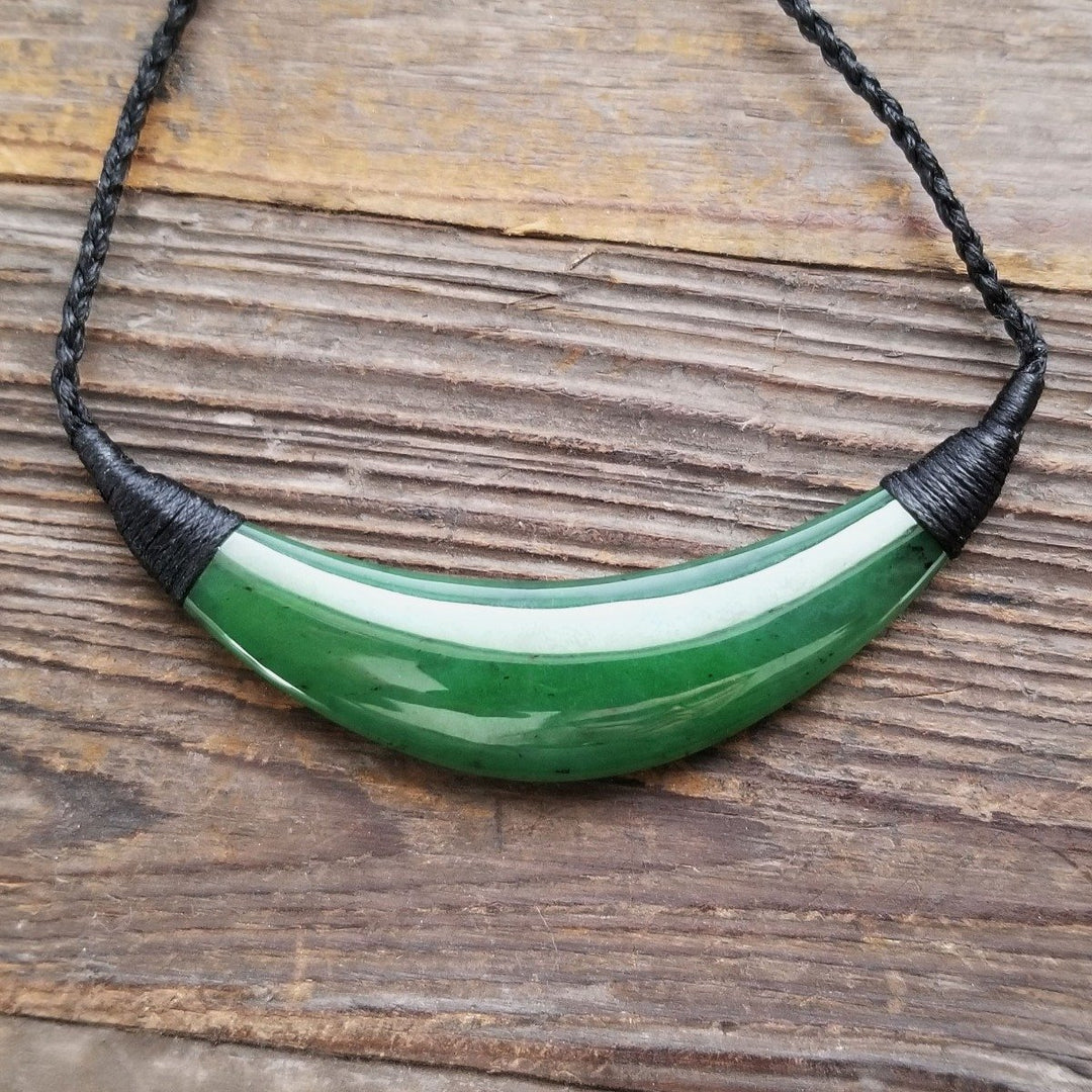 Green jade crescent pendant with a white stripe on a black braided cord
