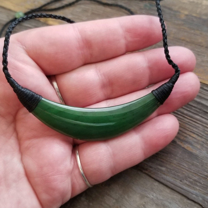 Close up of a green jade crescent pendant held in hand on a black cord