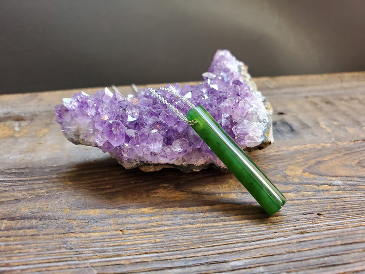 Green jade pendant on a silver chain resting against a purple amethyst cluster.