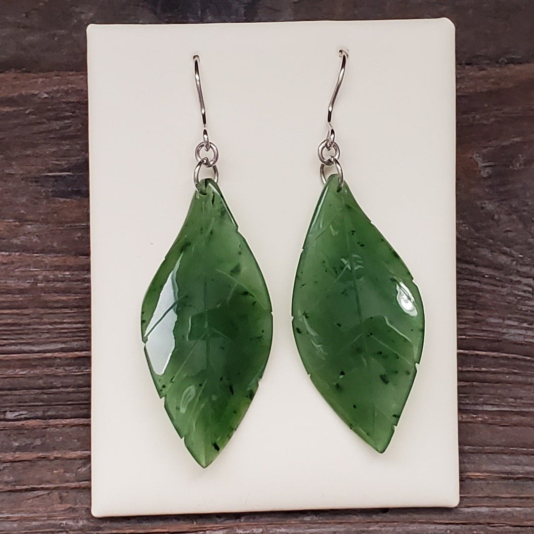 Jade leaf earrings displayed on a white card, large glossy green leaves with dark specks.