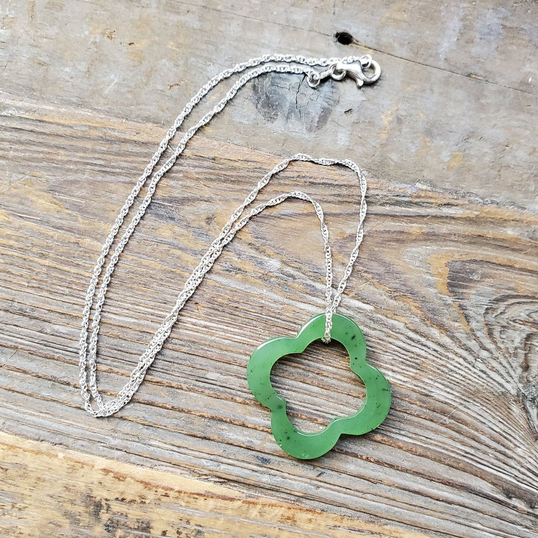 Green clover pendant on a silver chain laid on a wooden surface.