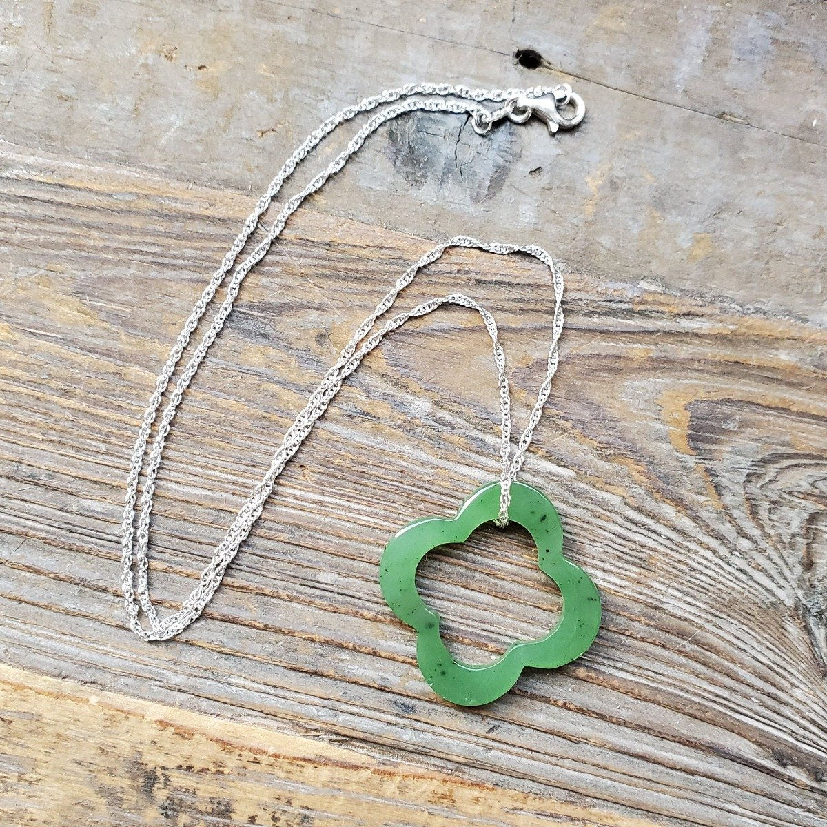 Green clover pendant on a silver chain laid on a wooden surface.