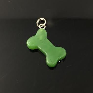 Green dog bone charm with a small metal loop at the top against a dark background.