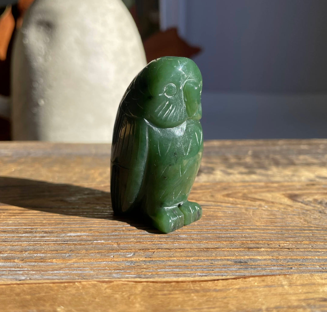 Green jade owl figurine with carved feather patterns on a wooden surface