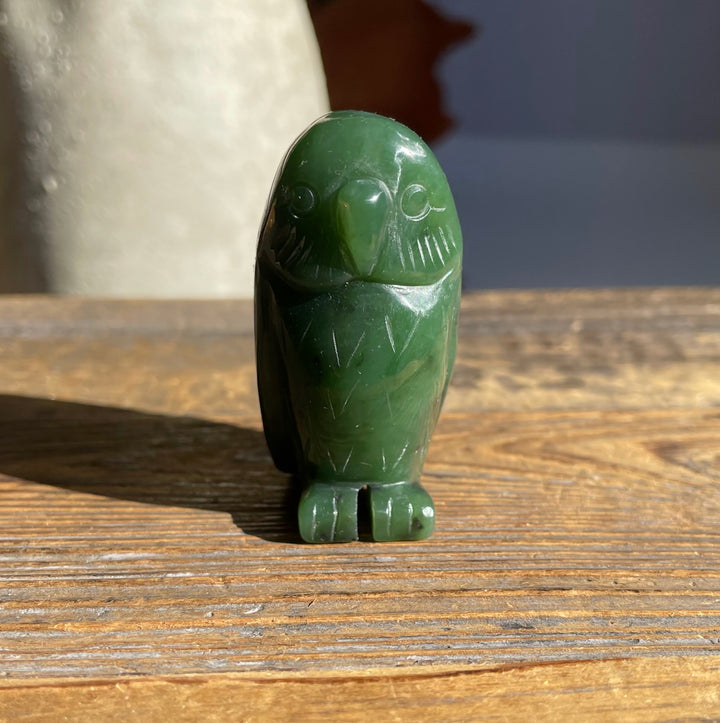 Side view of a green jade owl figurine with carved feathers standing on a wooden surface