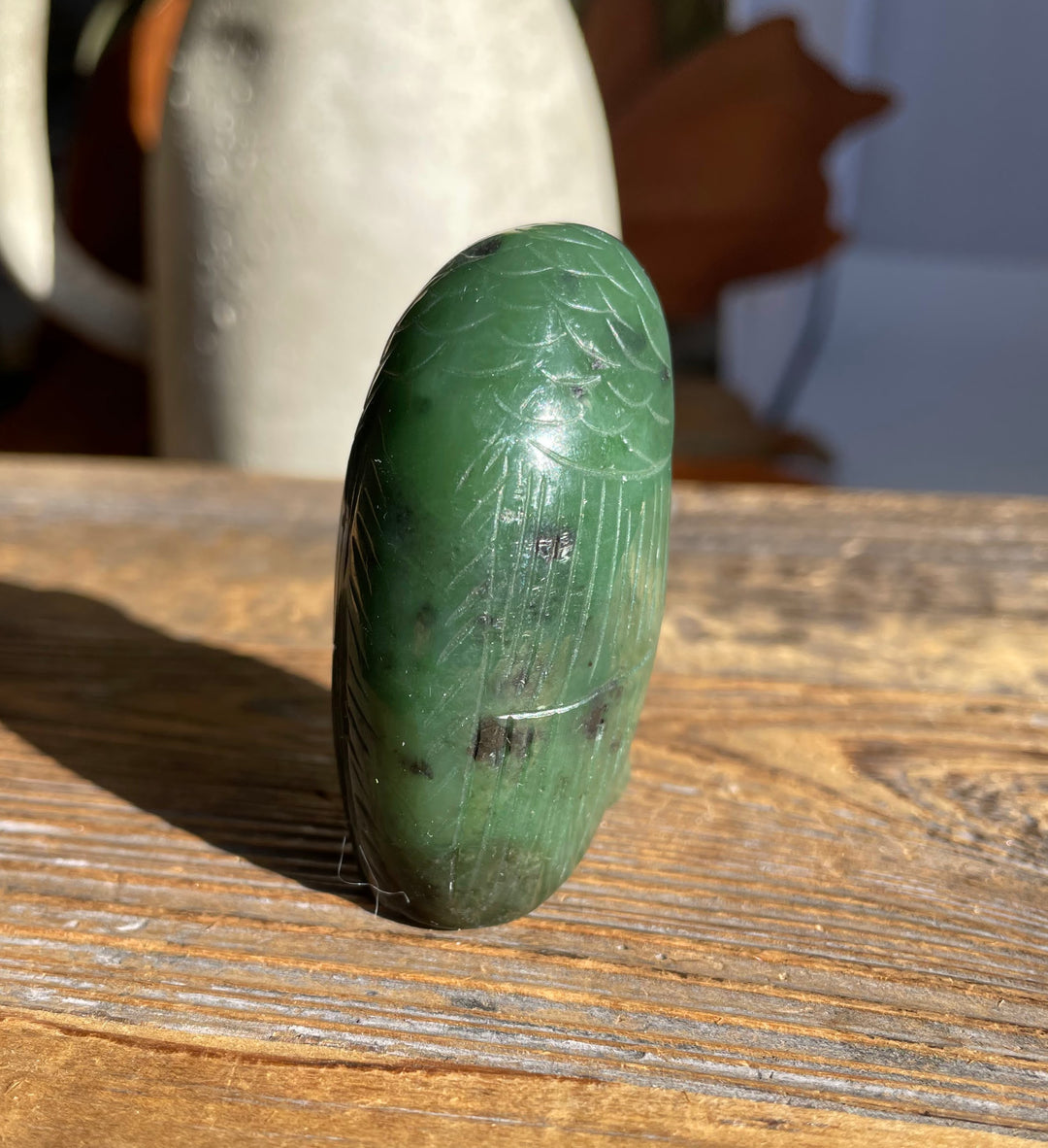Close side profile of the green jade owl showing etched feather lines on a wooden table