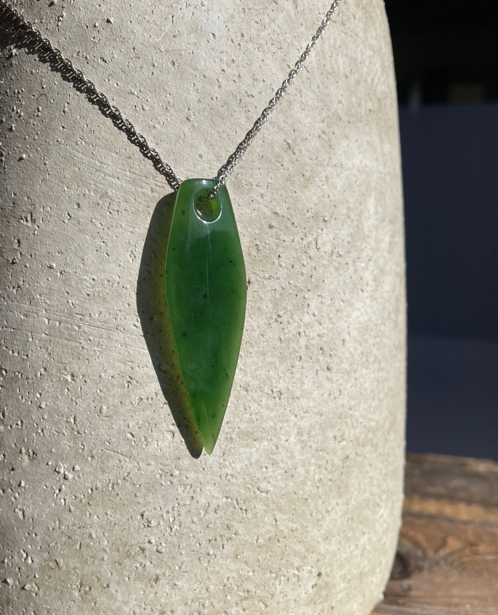 Large green drop shaped pendant hanging from a silver chain against a textured stone background.