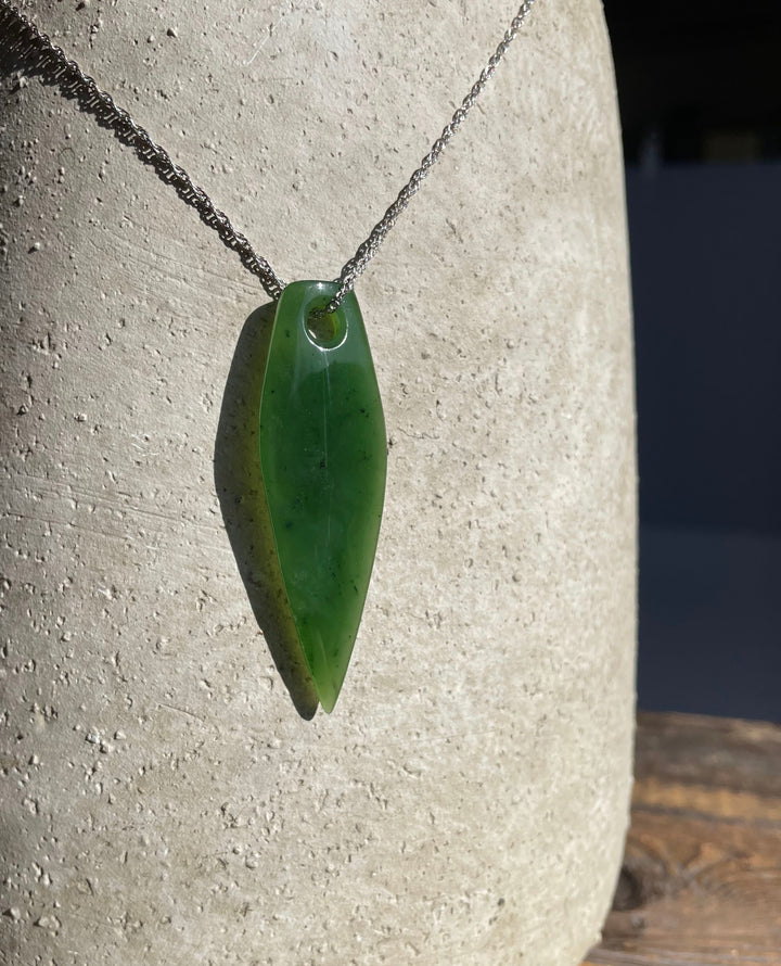 Large green drop shaped pendant hanging from a silver chain against a textured stone background.