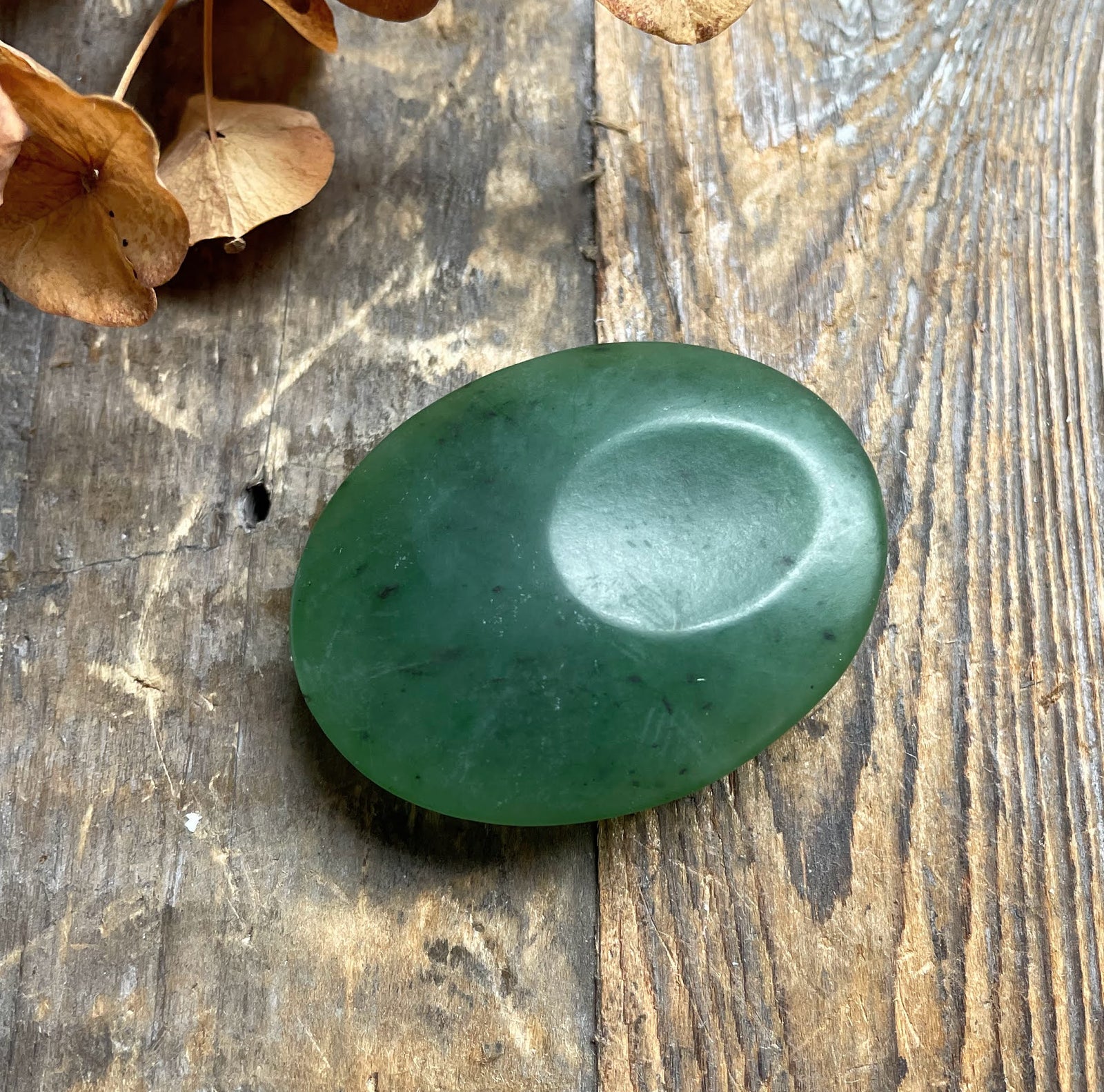 Oval satin finish green jade worry stone resting on a weathered wooden surface.
