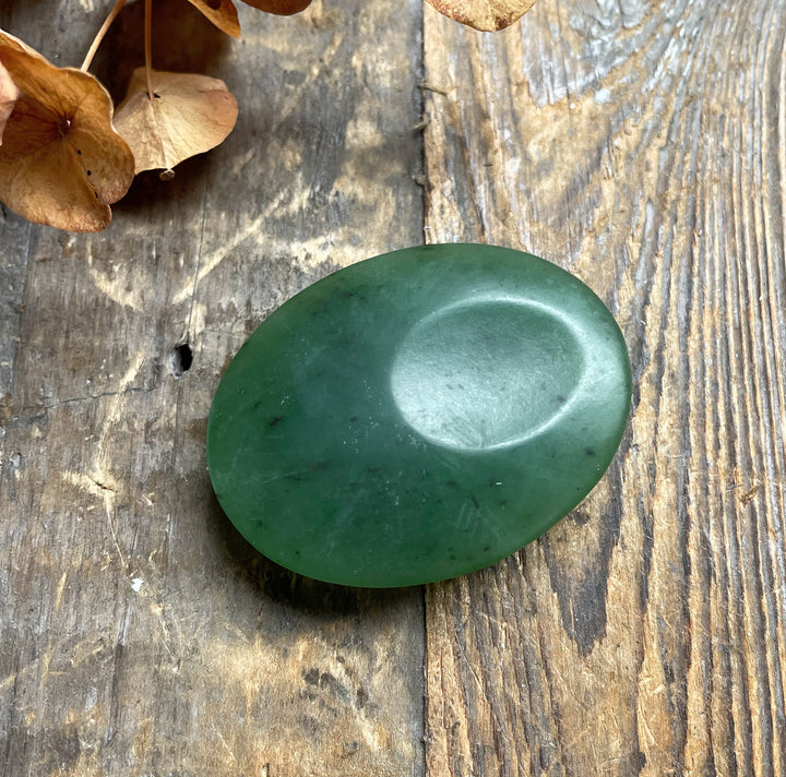 Oval satin finish green jade worry stone resting on a weathered wooden surface.