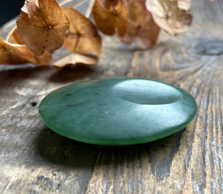 Green jade worry stone 1.75 inch satin finish on weathered wood with dried brown hydrangea blossoms in the background.