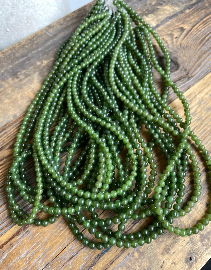 Several strands of 4mm nephrite jade beads in green hues on a wooden surface