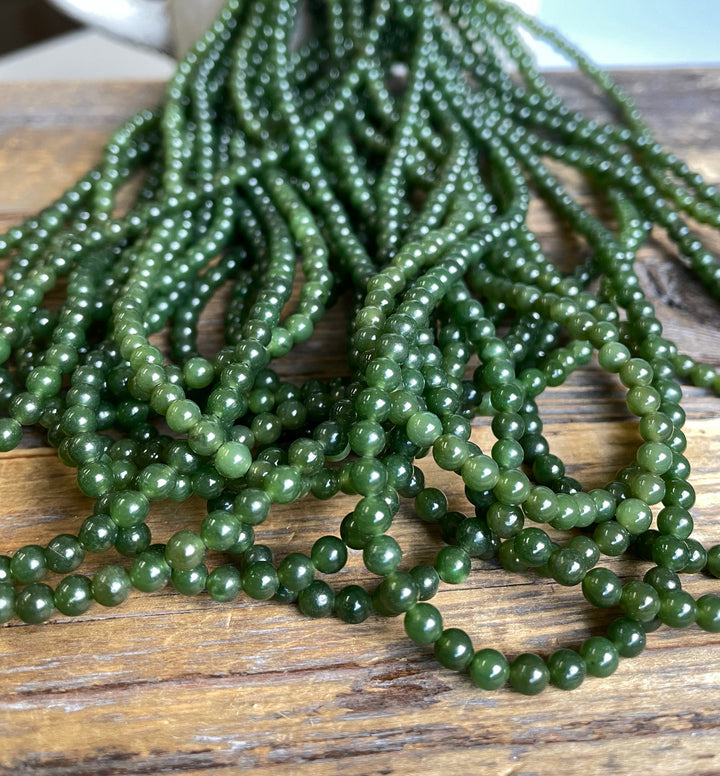 Close up of 4mm nephrite jade beads in varying green tones piled on a wooden surface