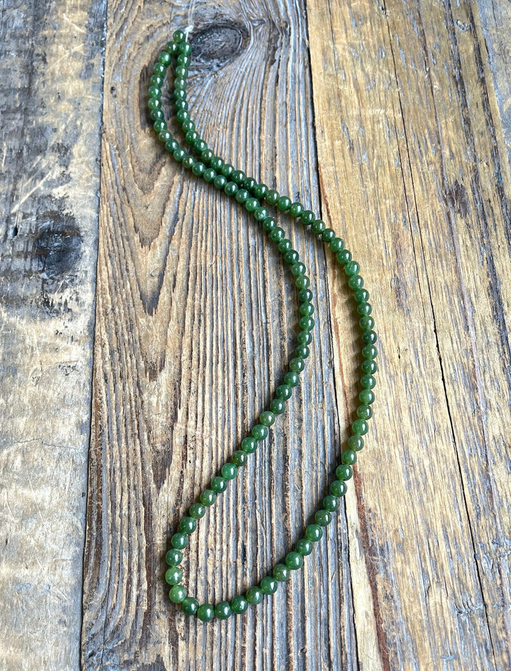Two strands of 4mm nephrite jade beads on a rustic wooden surface