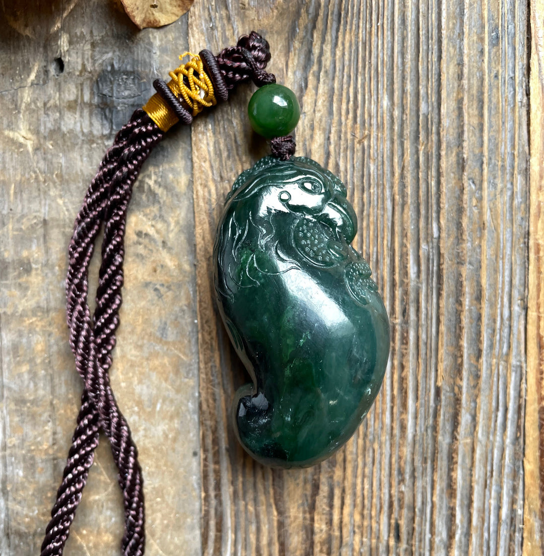 Dark green jade rooster pendant with carved feather details on a maroon braided cord with a green bead