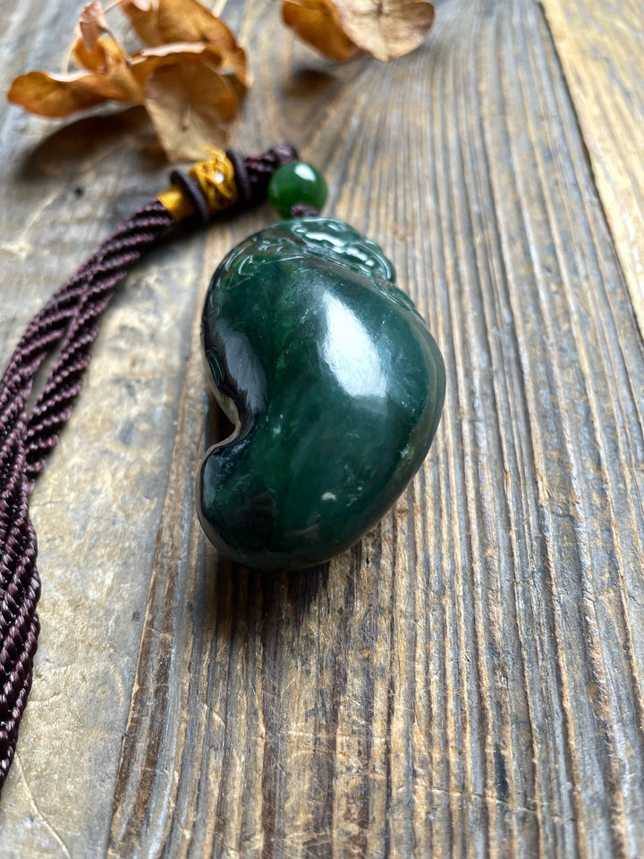 Green jade rooster pendant with a smooth curved form and carved details placed on a wooden surface