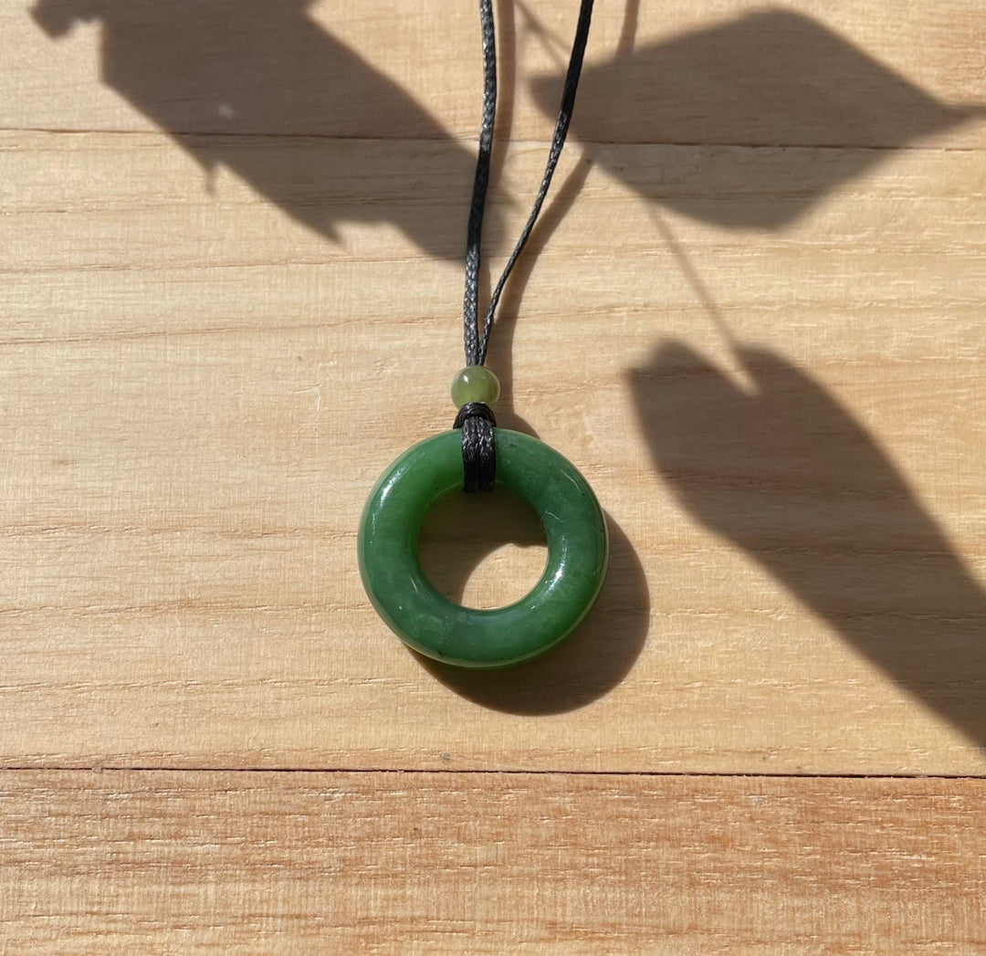 Round nephrite jade donut pendant 25mm on a black cord with a pale green bead above