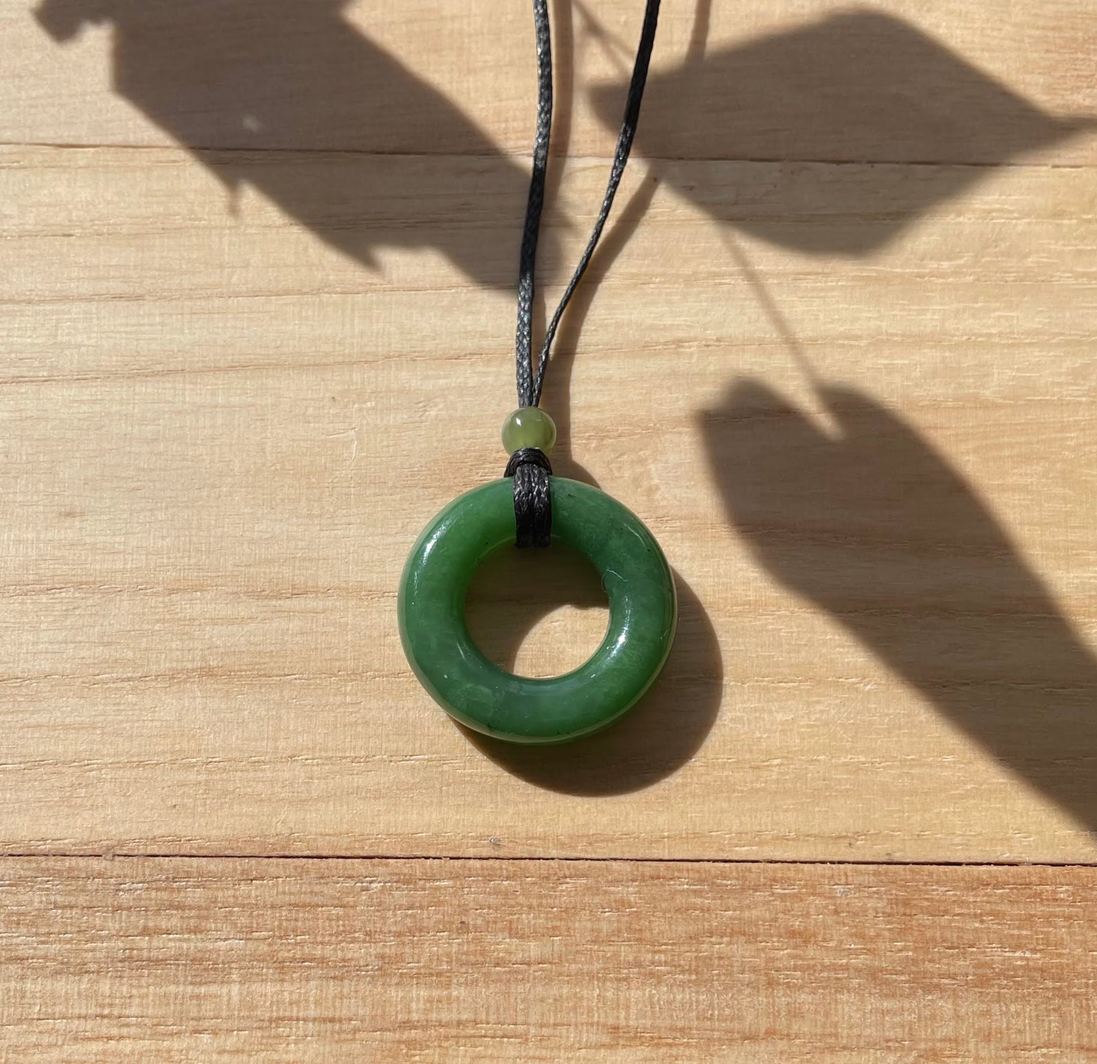 Round nephrite jade donut pendant 25mm on a black cord with a pale green bead above