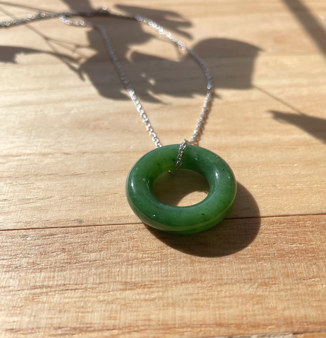 Green nephrite jade round donut pendant with silver chain resting on a wooden surface