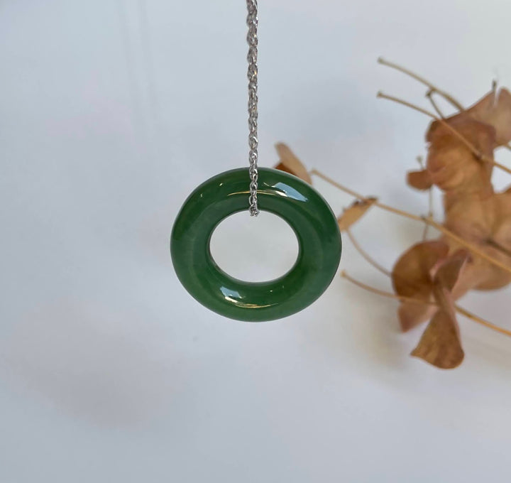 25mm nephrite jade round donut pendant suspended by a silver chain against a pale background with dried leaves