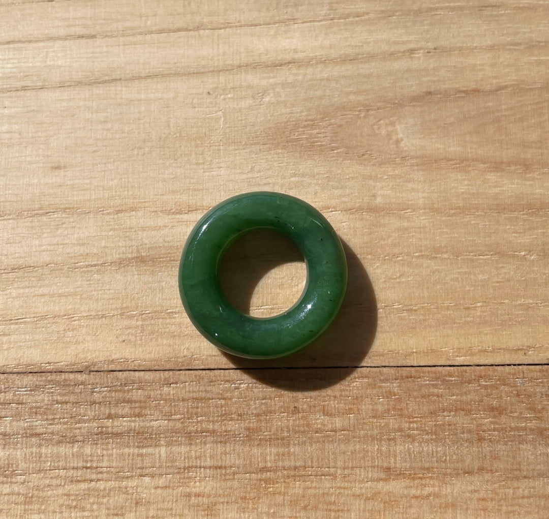 Green nephrite jade donut pendant on a silver chain displayed on a wooden background