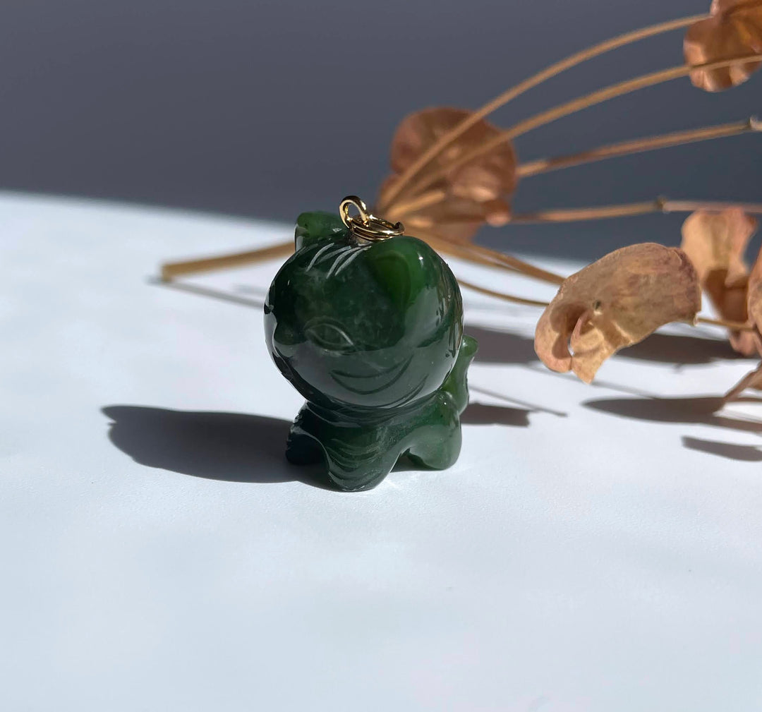 Side view of jade tiger charm resting on a white surface with dried plant stems in the background