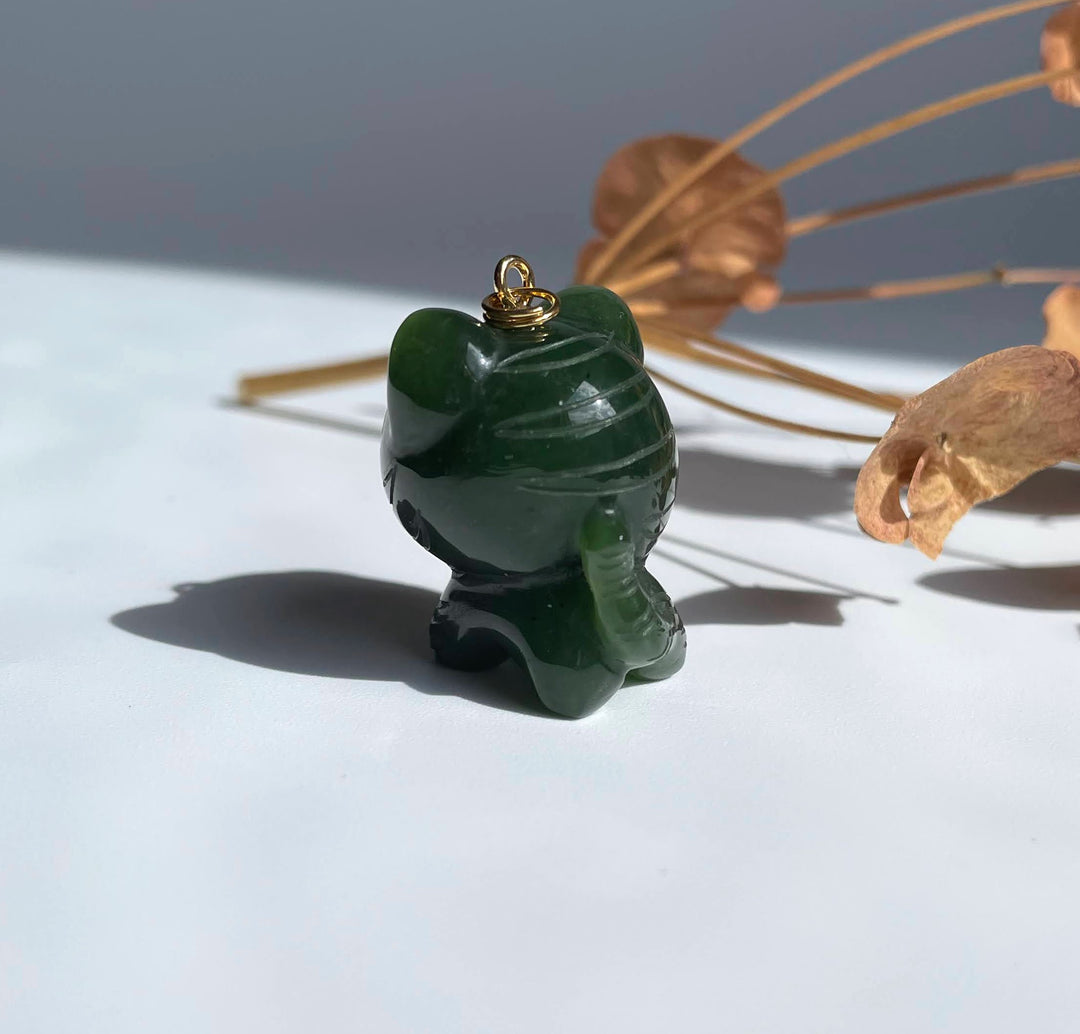 Close up of dark green jade tiger charm with a gold bail on top against a white surface