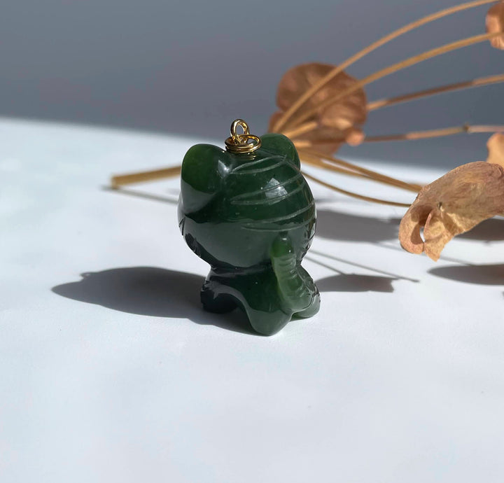 Close up of dark green jade tiger charm with a gold bail on top against a white surface