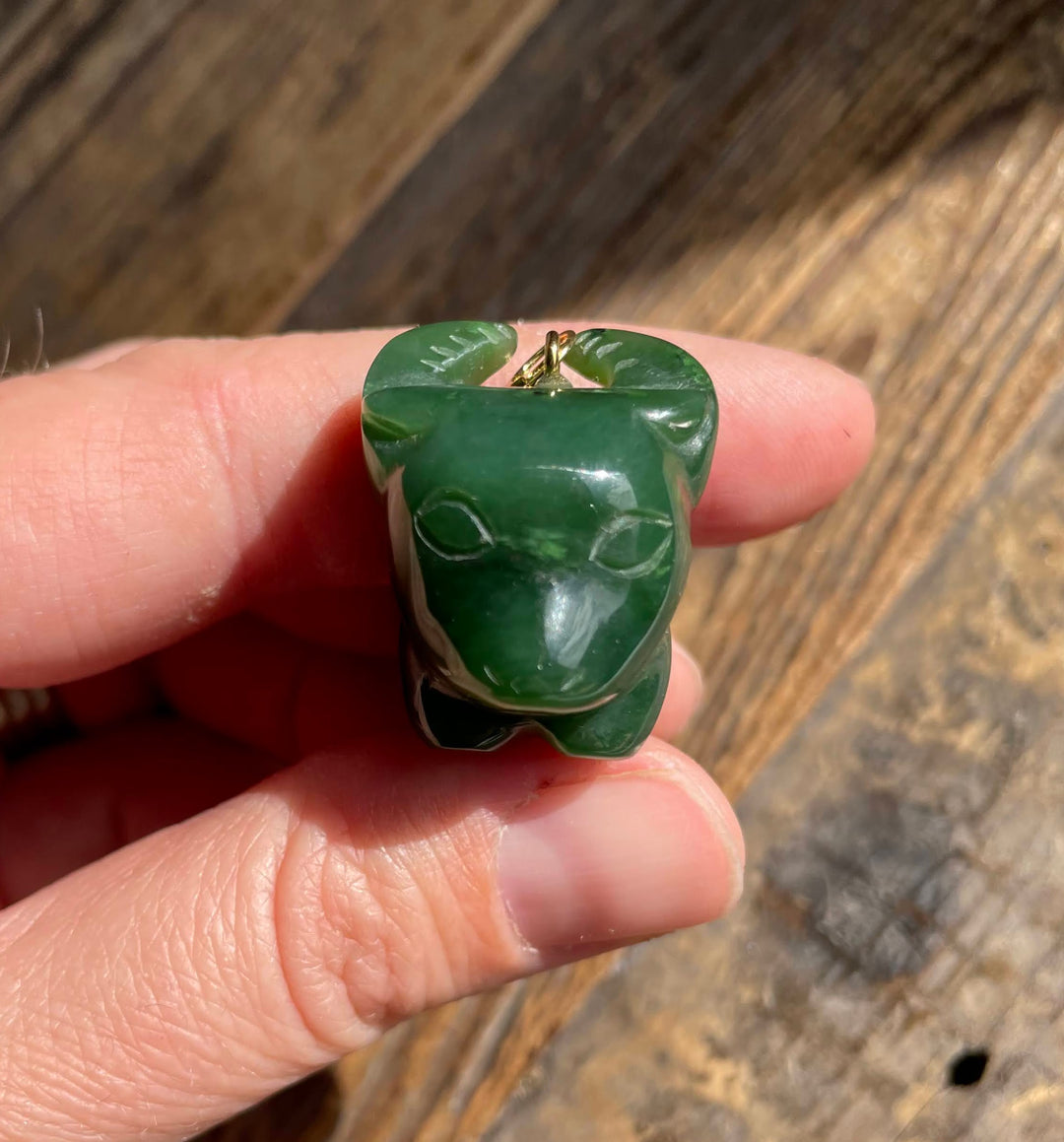 Green jade ox cartoon charm with a gold loop held between fingers