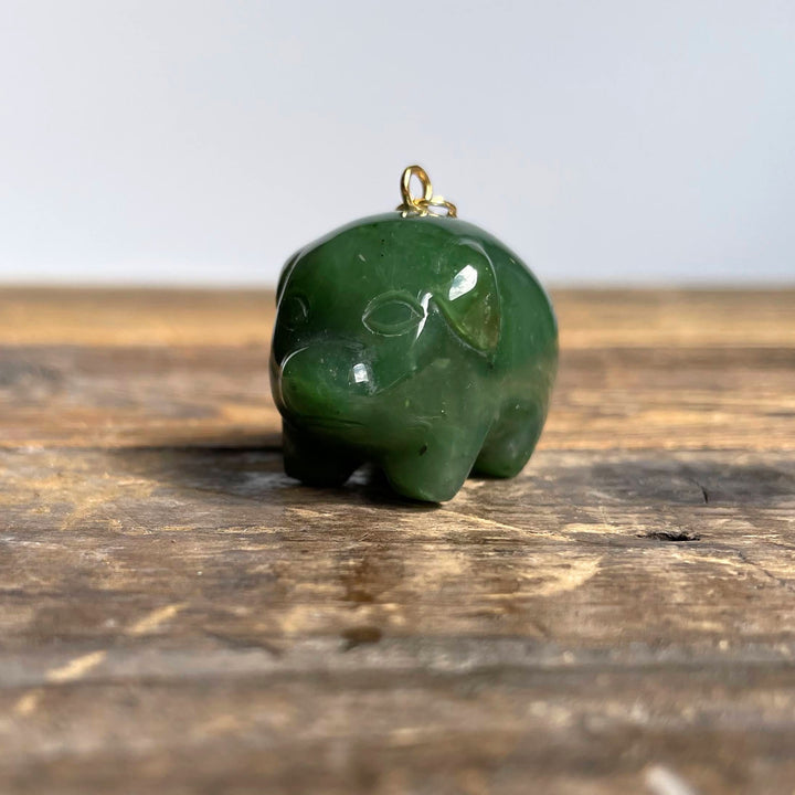 Green jade pig charm with a gold loop on top resting on a wooden surface.