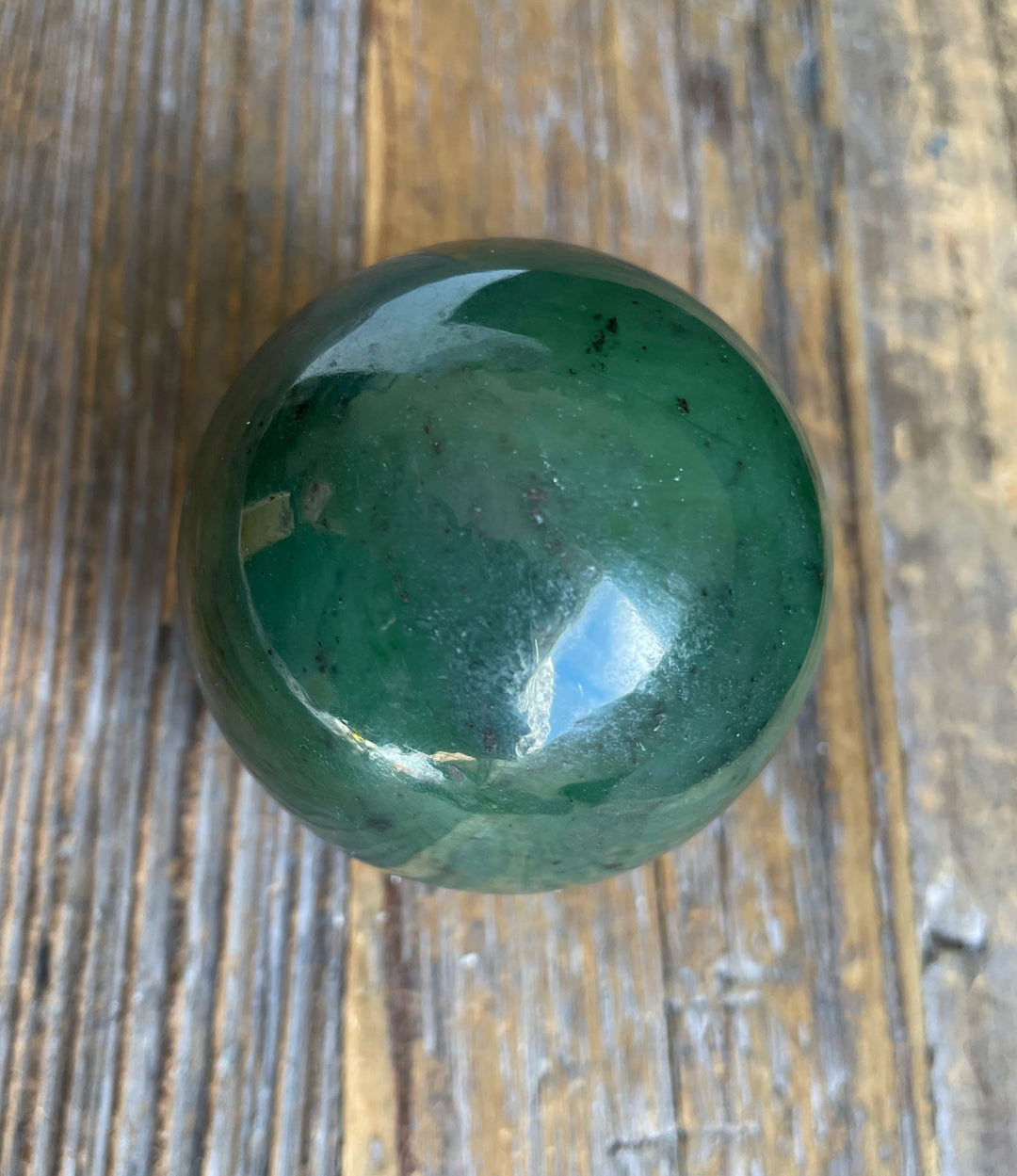 Polished Canadian jade sphere 50mm on a wooden surface.