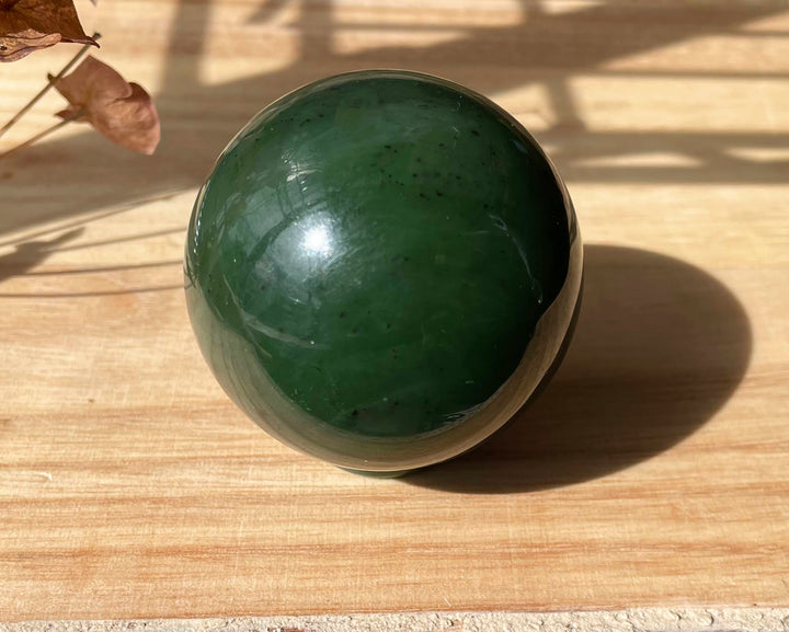 Canadian Jade Sphere 50mm viewed at an oblique angle on a wooden surface with sunlight